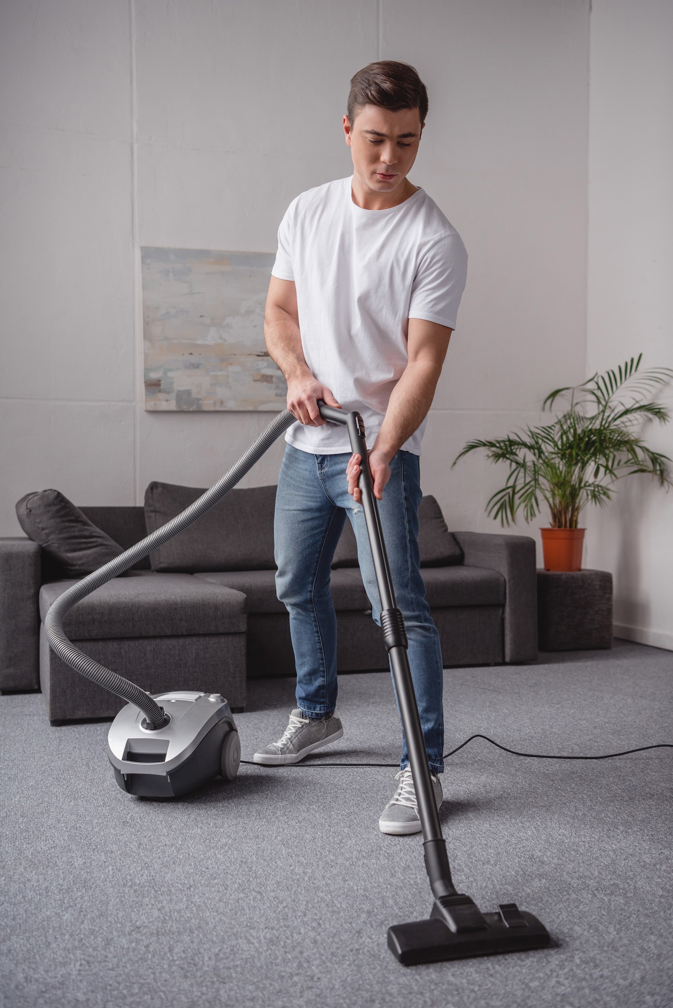 handsome man cleaning carpet in living room with vacuum cleaner